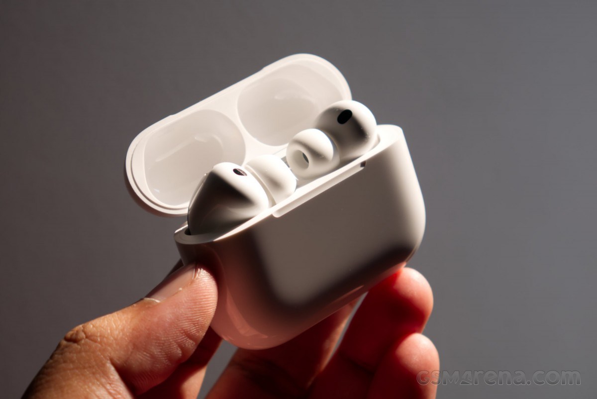 White wireless earbuds in a charging case held in a hand, case lid open to reveal both earbuds