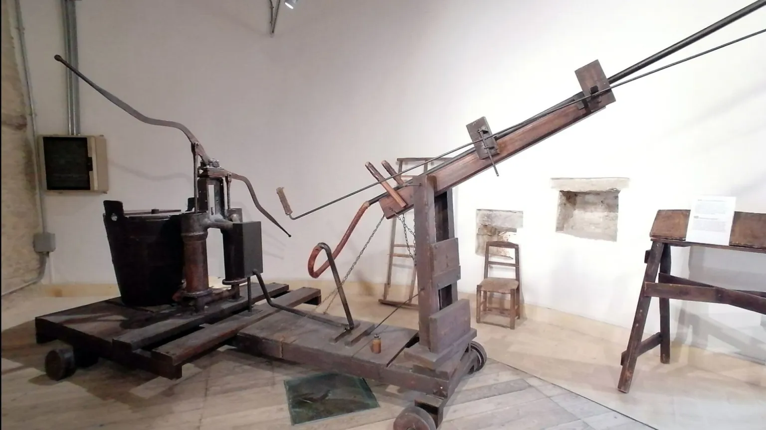Old wooden mechanical press on a wheeled base in a museum exhibit area.